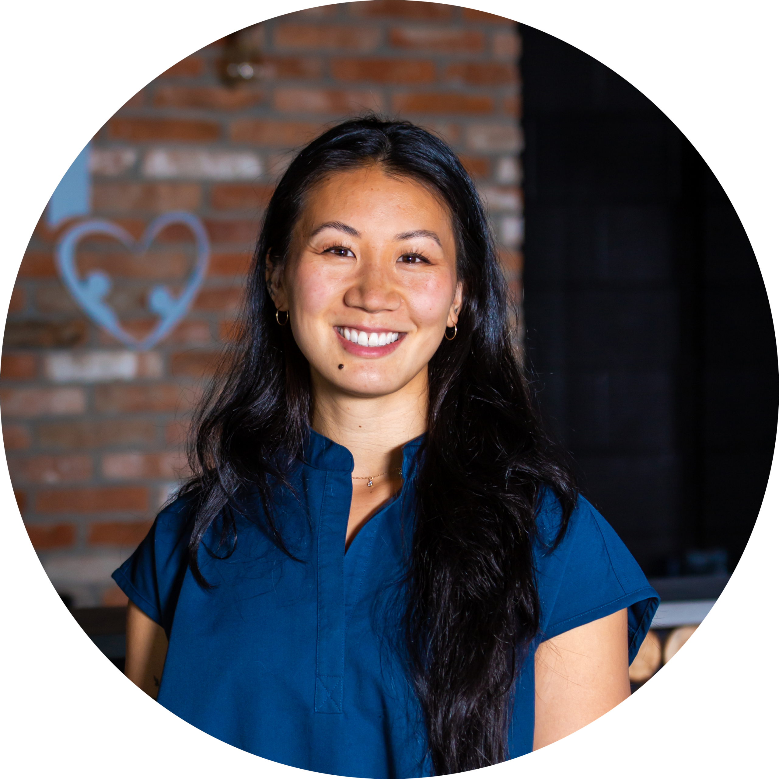 A woman in a blue shirt smiling in front of a brick wall.
