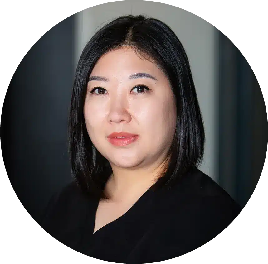A member of Our Team, a woman with straight, shoulder-length black hair and light makeup, wears a black top and looks at the camera with a neutral expression.
